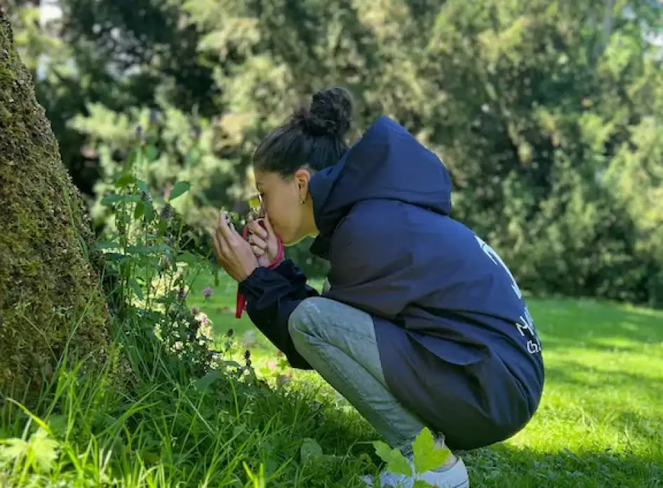 une jeune femme entrain de sentir des herbes au pied d'un arbre