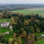 Vue aérienne d'une ancienne ruine du château entouré d'arbres et de champs verts luxuriants sous un ciel couvert.